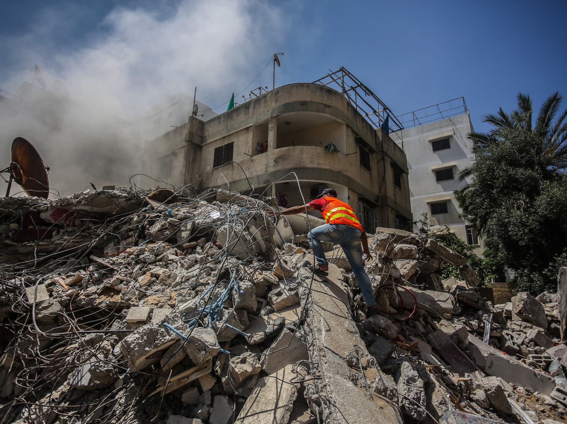 A man climbing on a pile of rubble that is still smoking after an air strike.