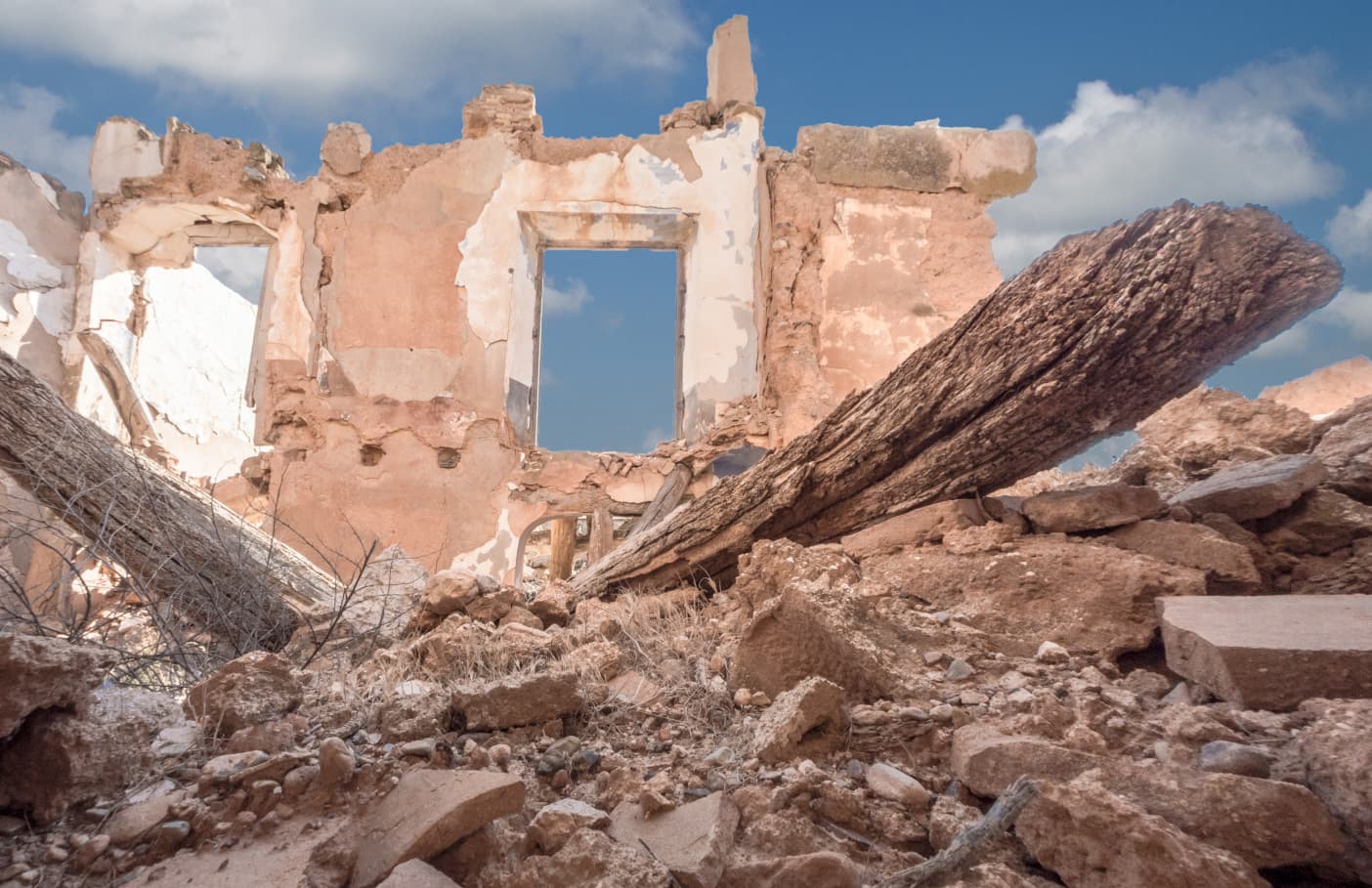 The rubble of a destroyed building and in the background a remains of a house wall.