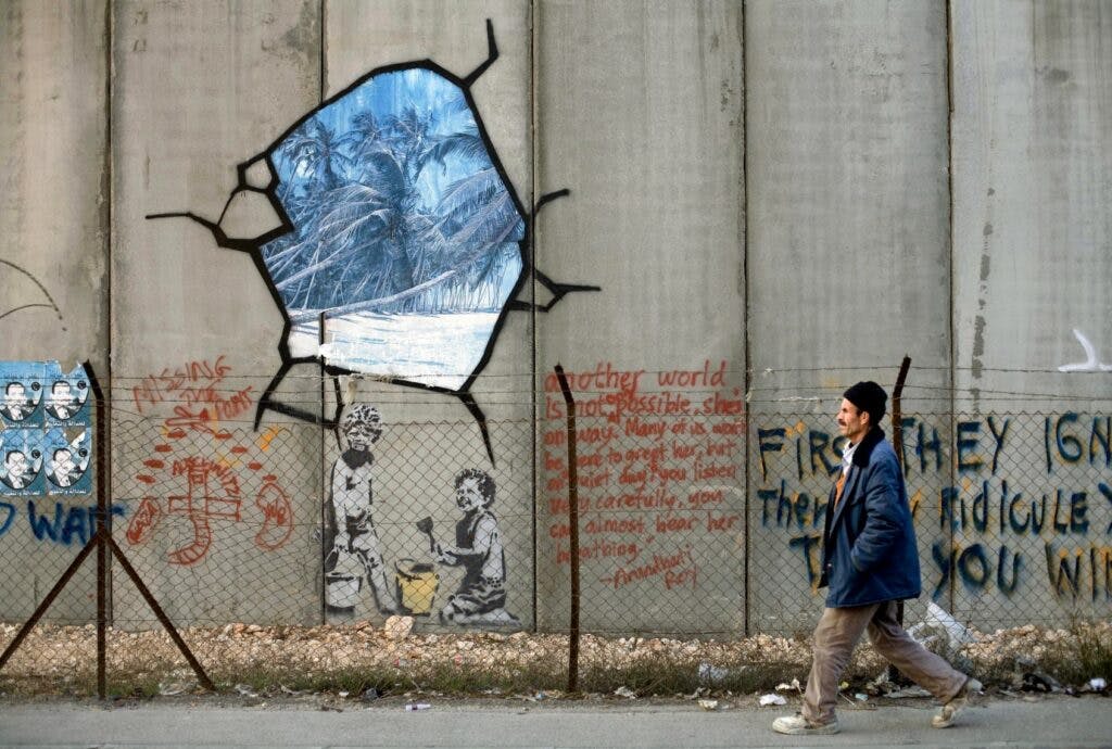 A man passes graffiti on a high wall.