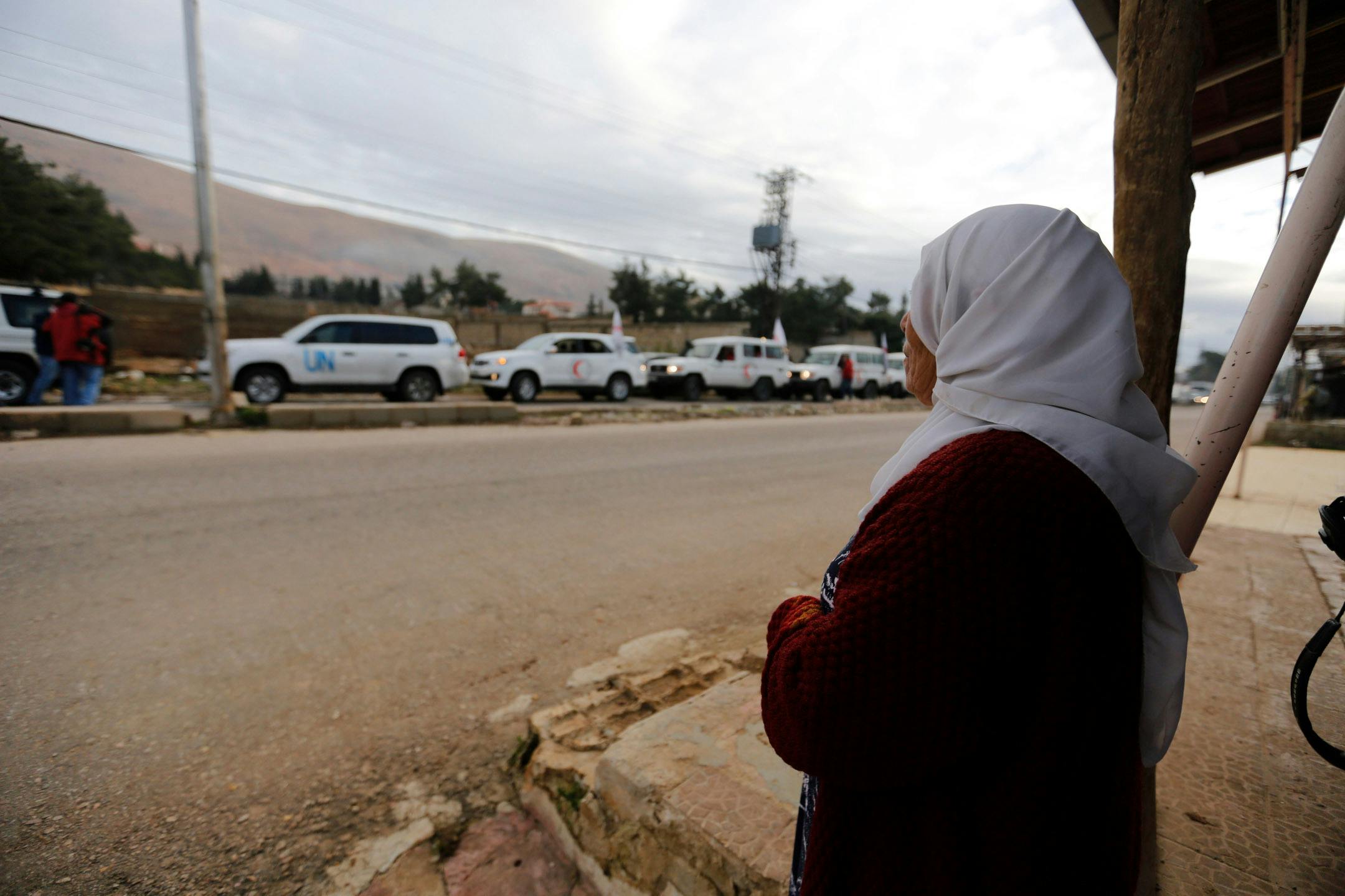 A woman watching United Nations vehicles, as part of a humanitarian convoy.