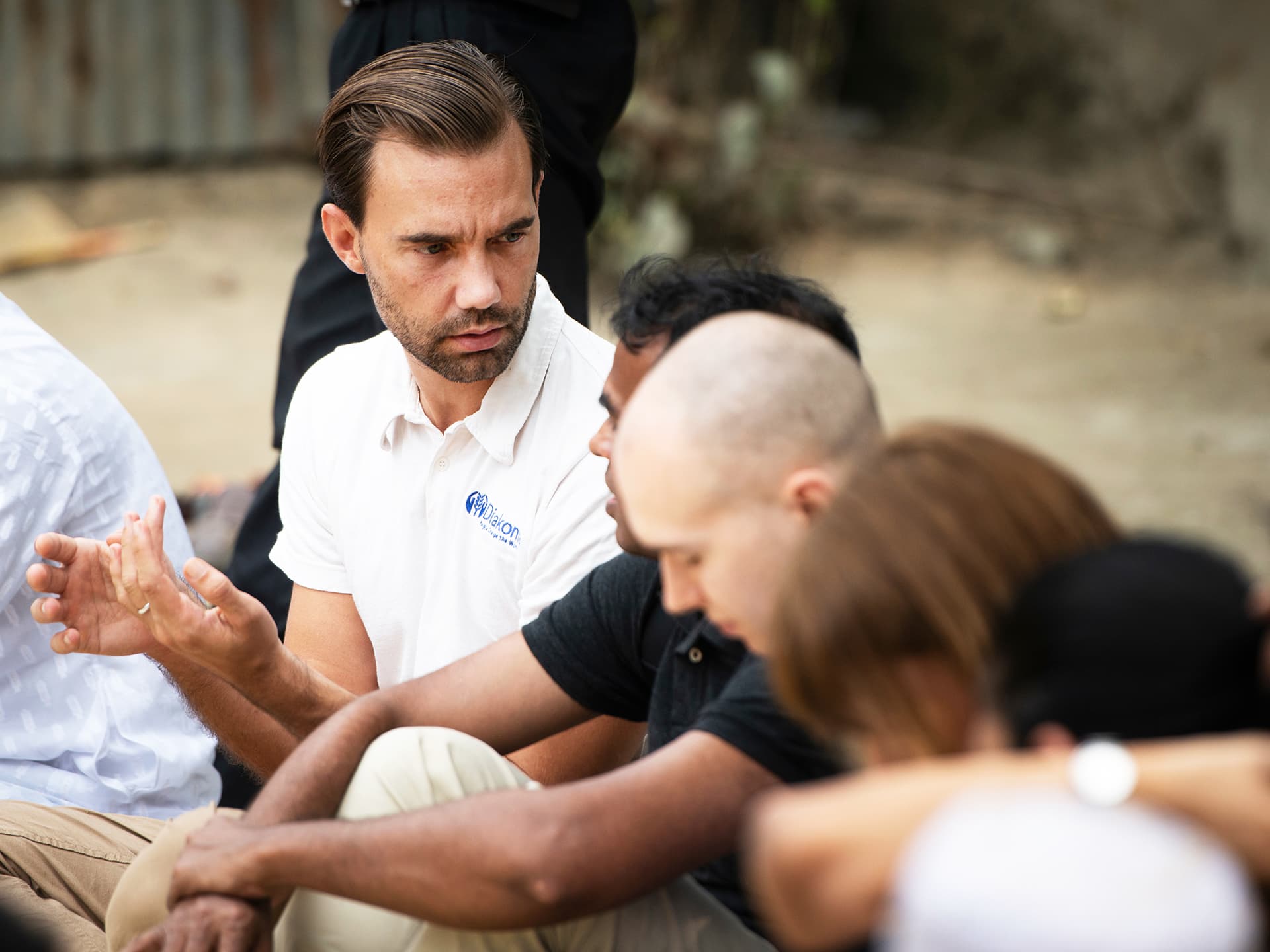 A man in a Diakonia t-shirt sitting with a group of people.