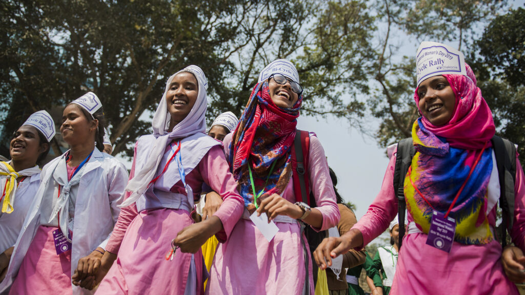 A group of young women at a manifestation. They are jolding hands and smiling.