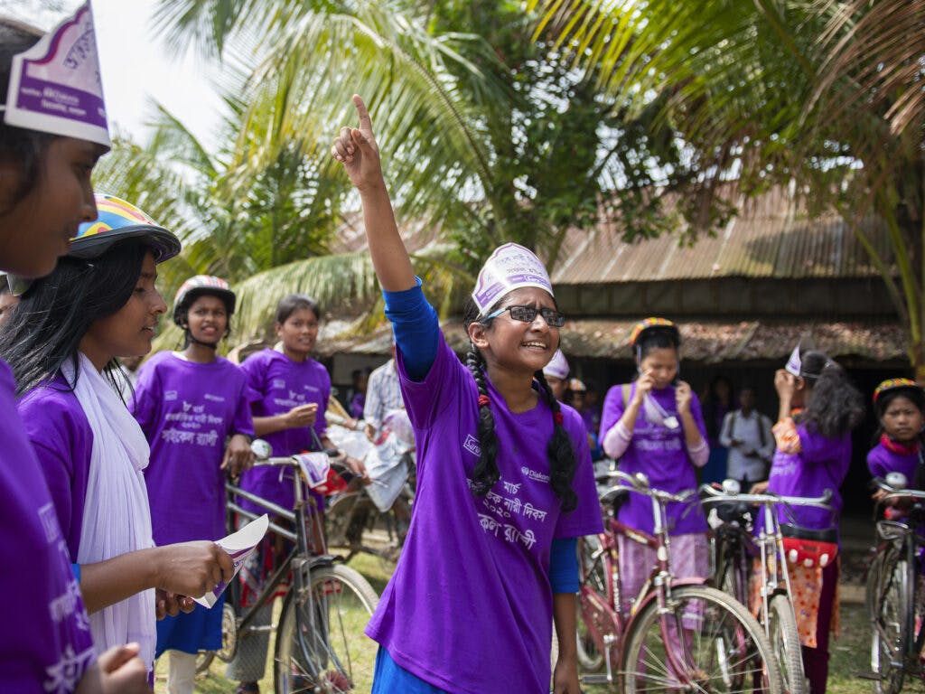 A group of girls at a bicycle rally in Bangladesh. One girl is lifting her hand up.