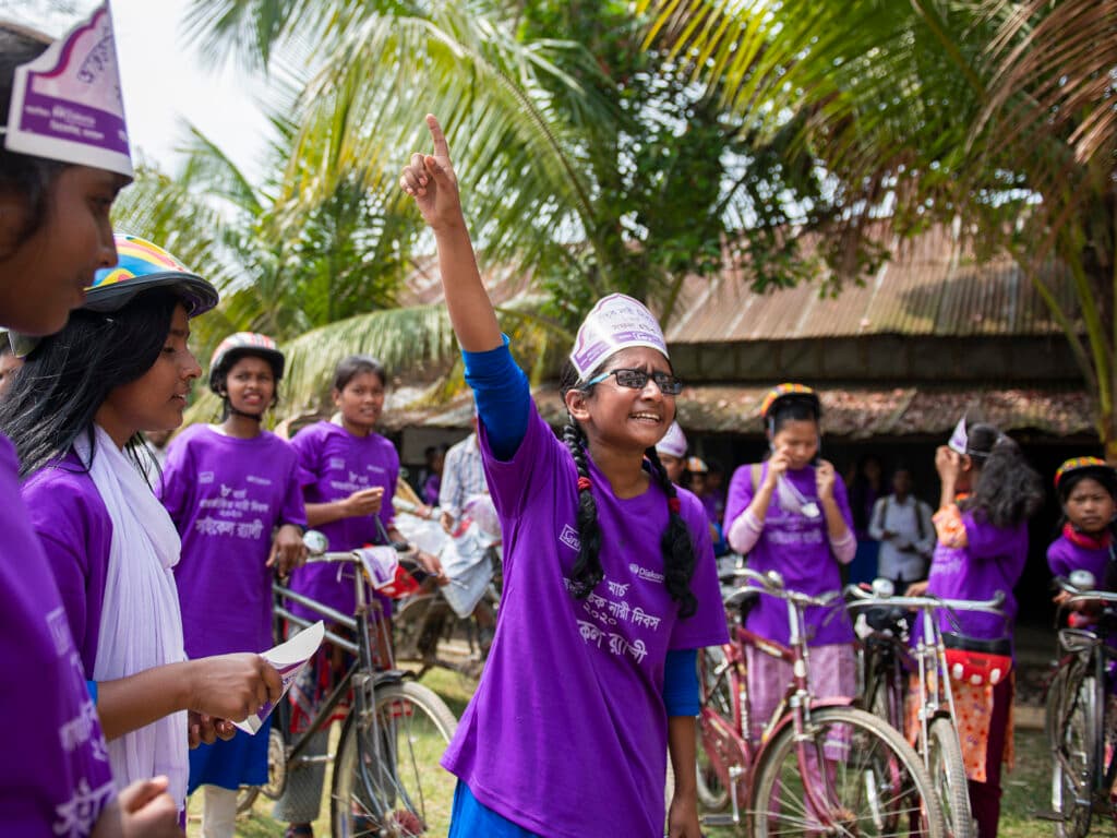 A group of girls at a bicycle rally in Bangladesh. One girl is lifting her hand up.