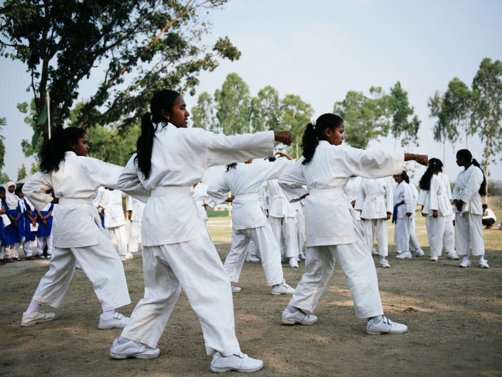 A large group of young women in white karate suits, standing in karate positions.