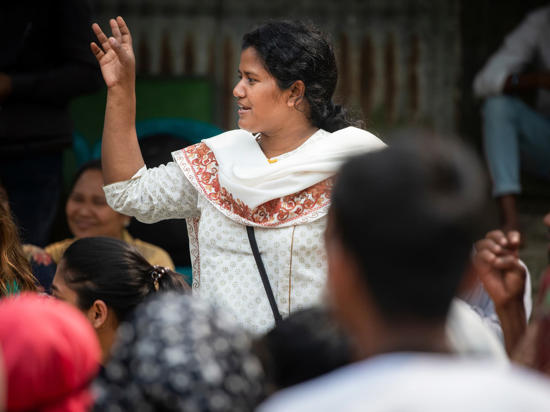 A woman standing in a group of people, gesticulating and talking.