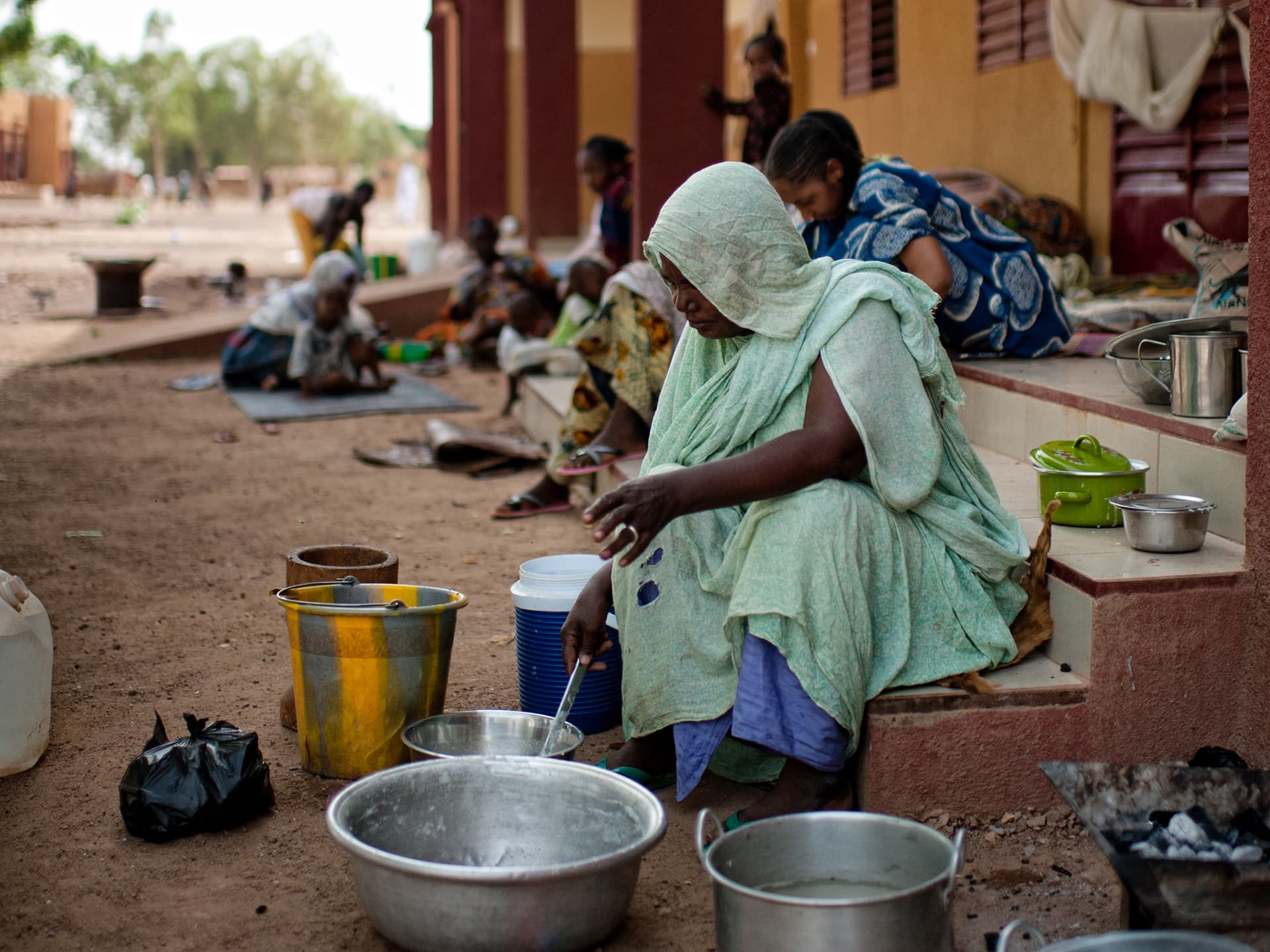 A woman wearing a head scarf sitting by some pots and pans on the ground.