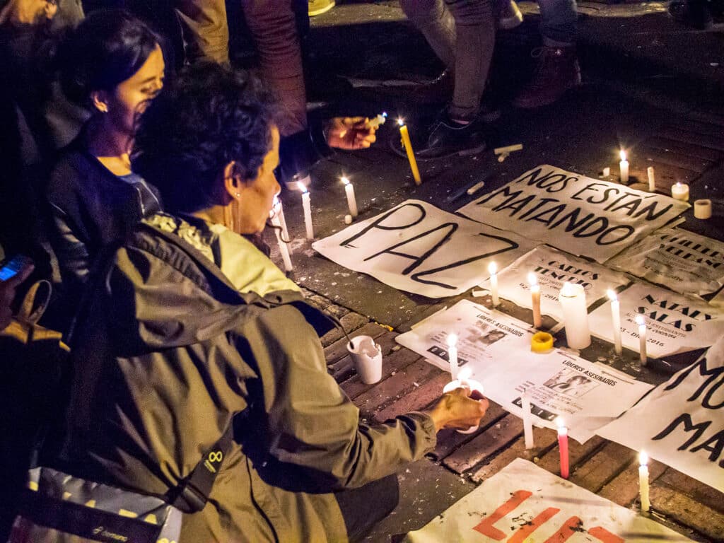 Two women lighting candles next to signs promoting peace.