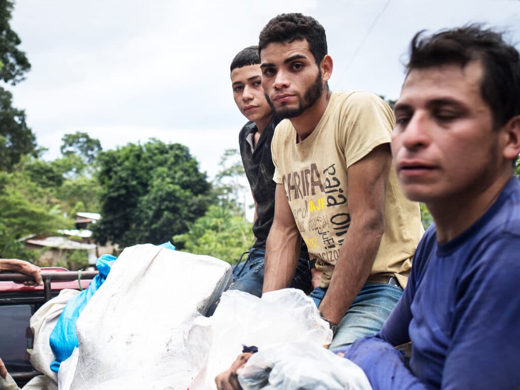 Three men sitting in an open truck with bags.