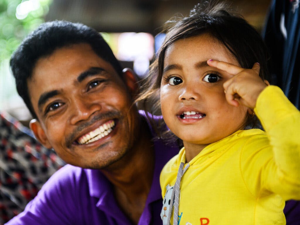 A closeup of a smiling Cambodian father next to his young daughter.