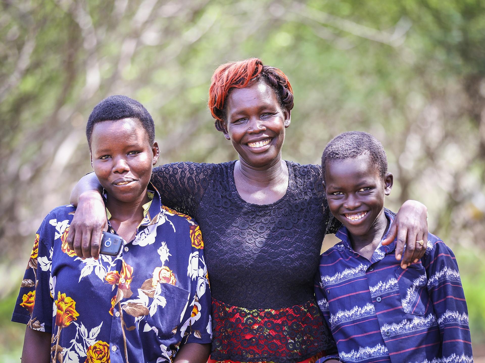 Kenyan mother holding her arms around two children with trees in the background.