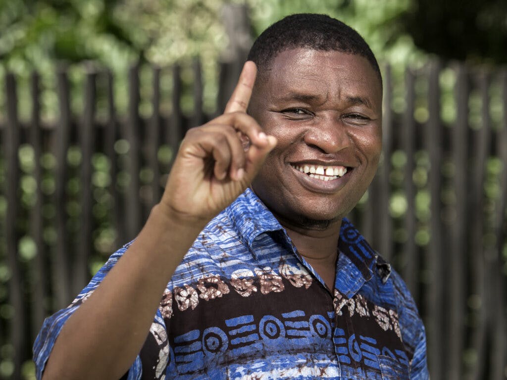 A smiling Kenyan man with his finger lifted, looking in to the camera.