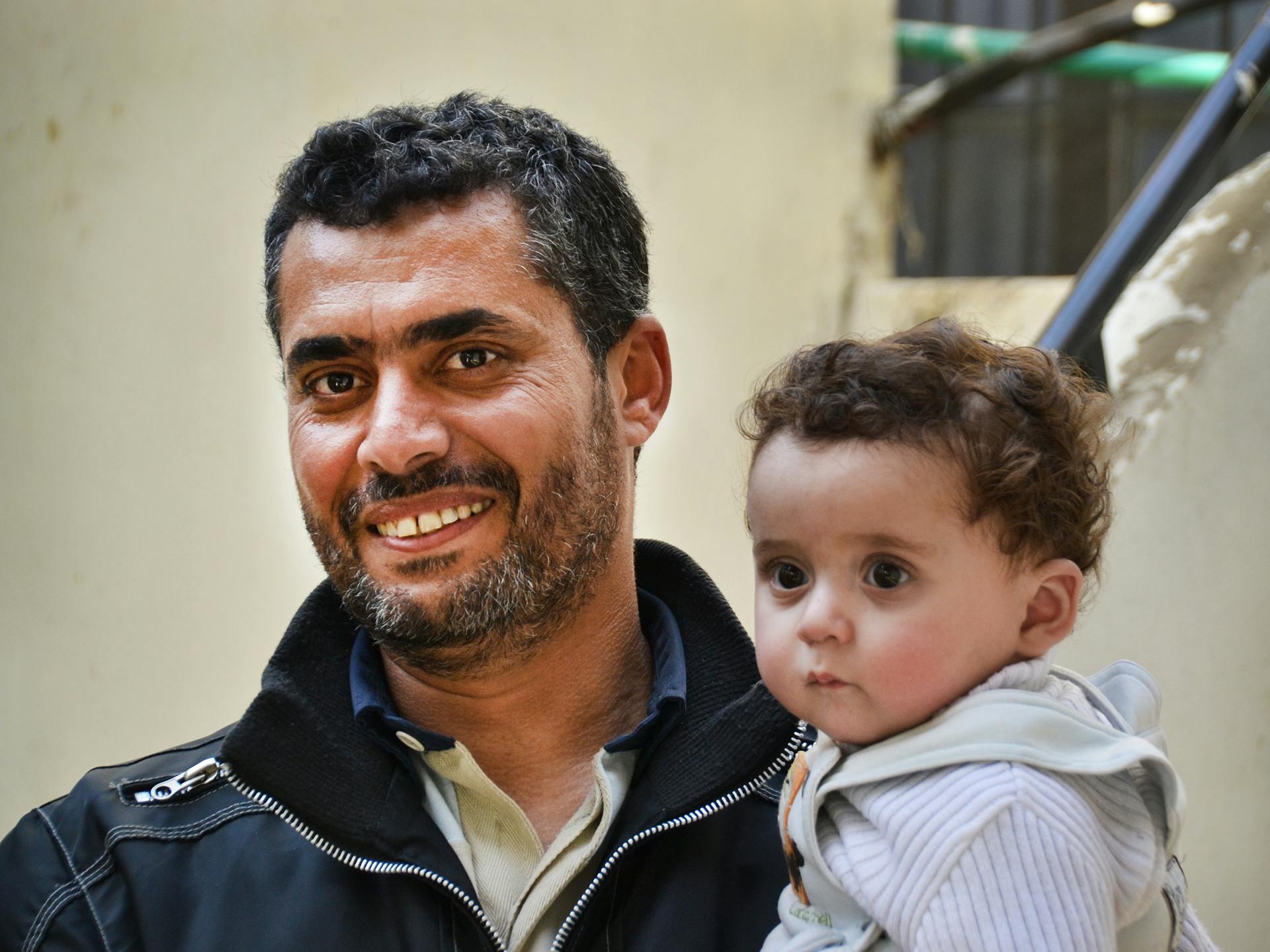 A bearded man smiling and holding a baby.