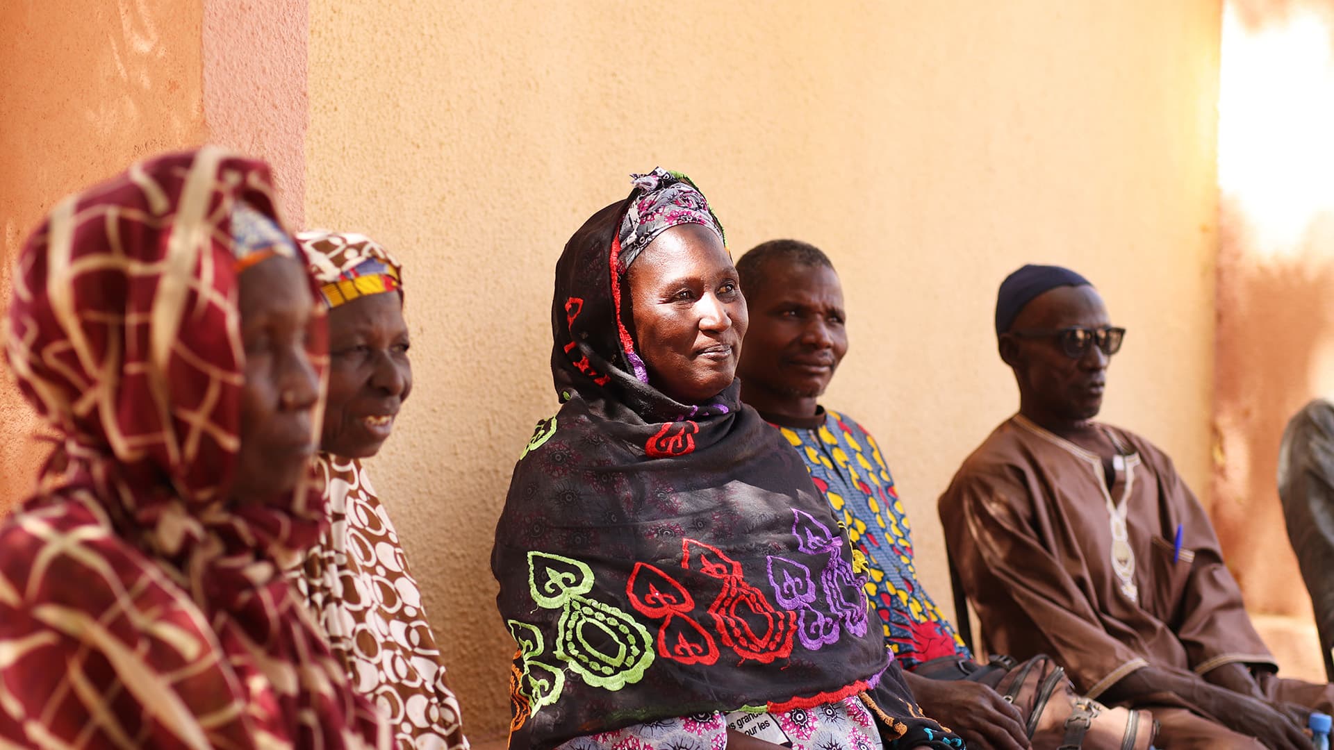 A woman sitting against a wall with a group of people.