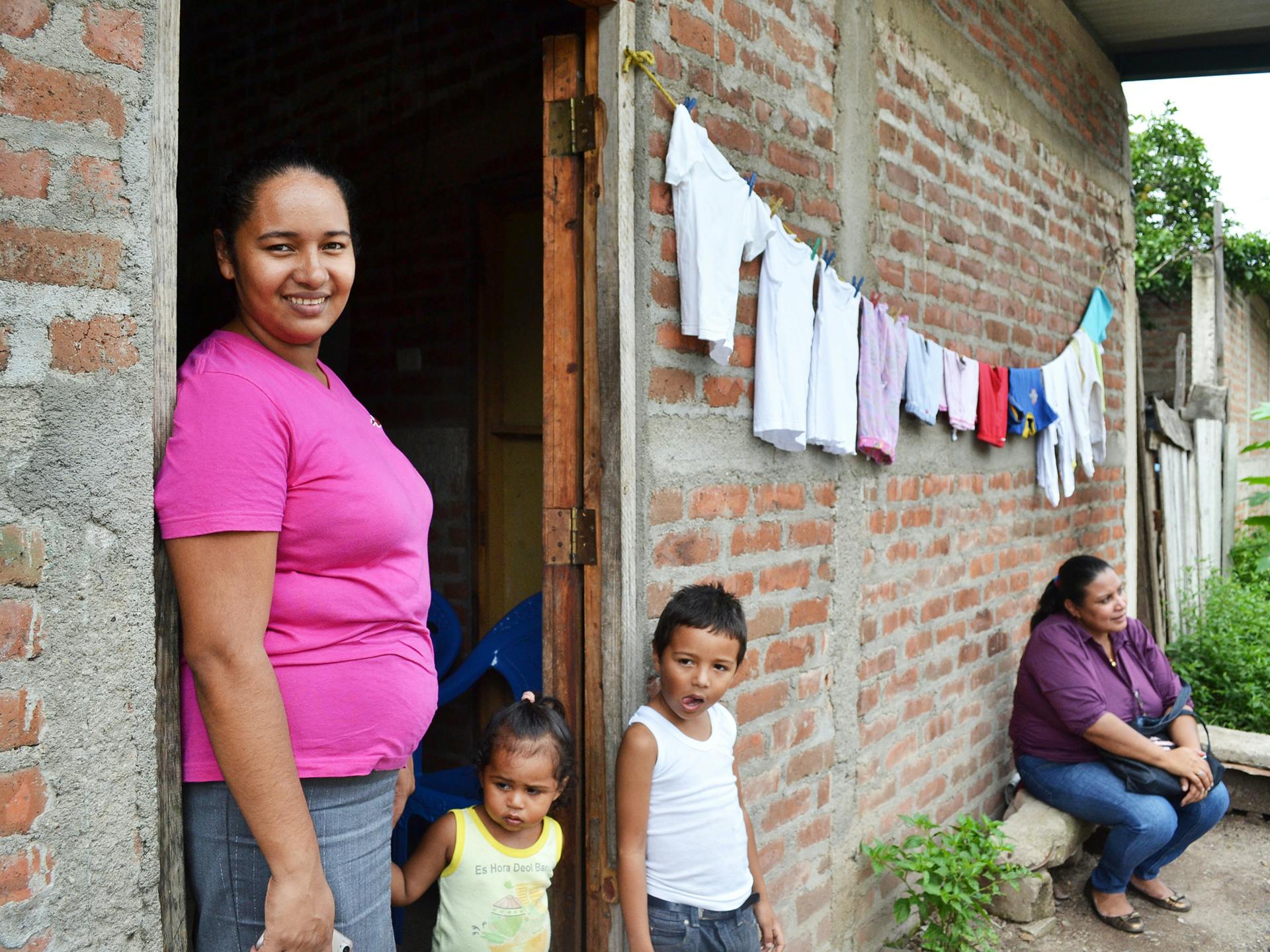 A Nicaraguan woman standing outside a house with two kids.
