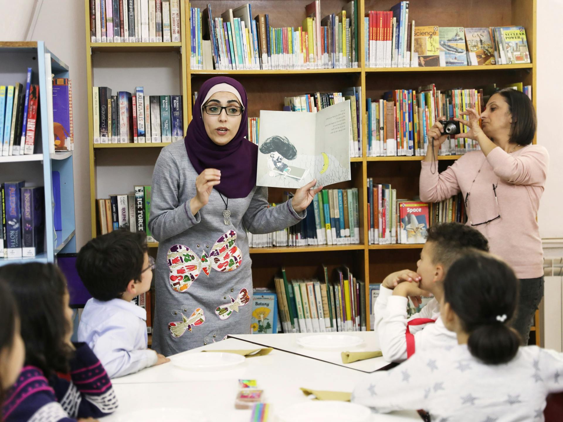 A teacher reading a childrens book to a group of children in a library