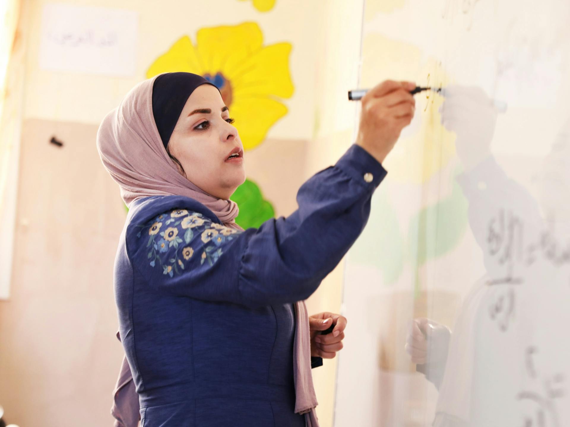 A woman wearing a hijab writing on a white board.