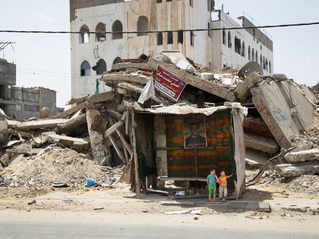 Bombed houses in Gaza. Two kids are sitting in a booth.
