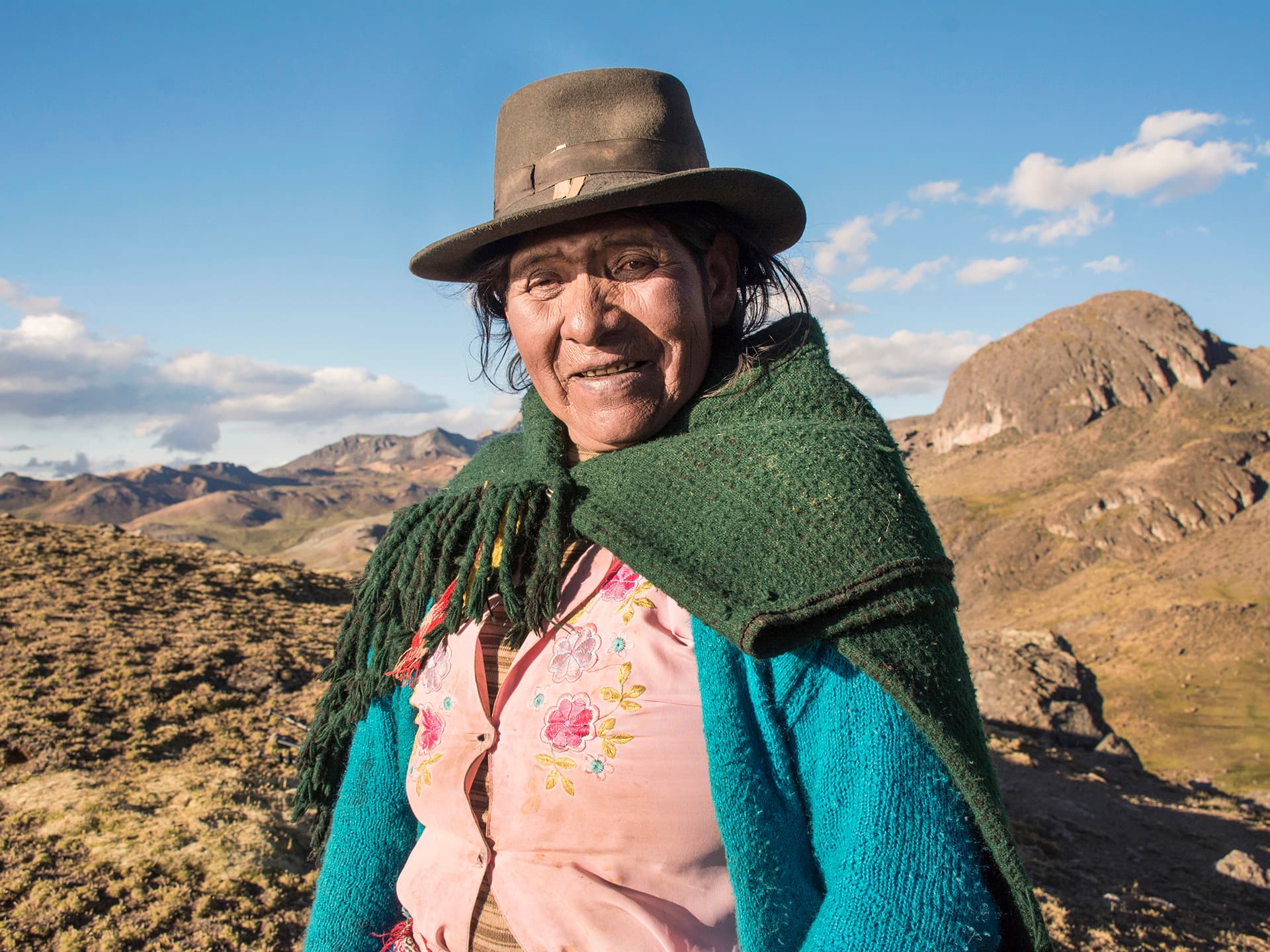 A Peruvian older woman wearing a hat and a knitted scarf.