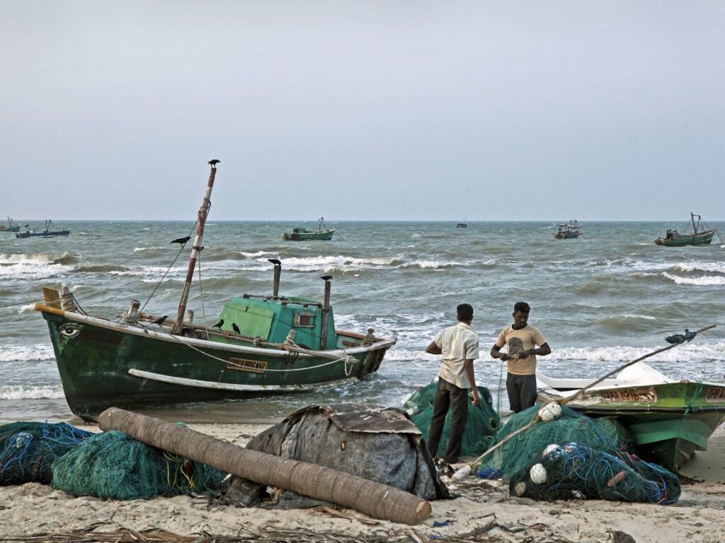 Two fishermen and a boat at the beach.