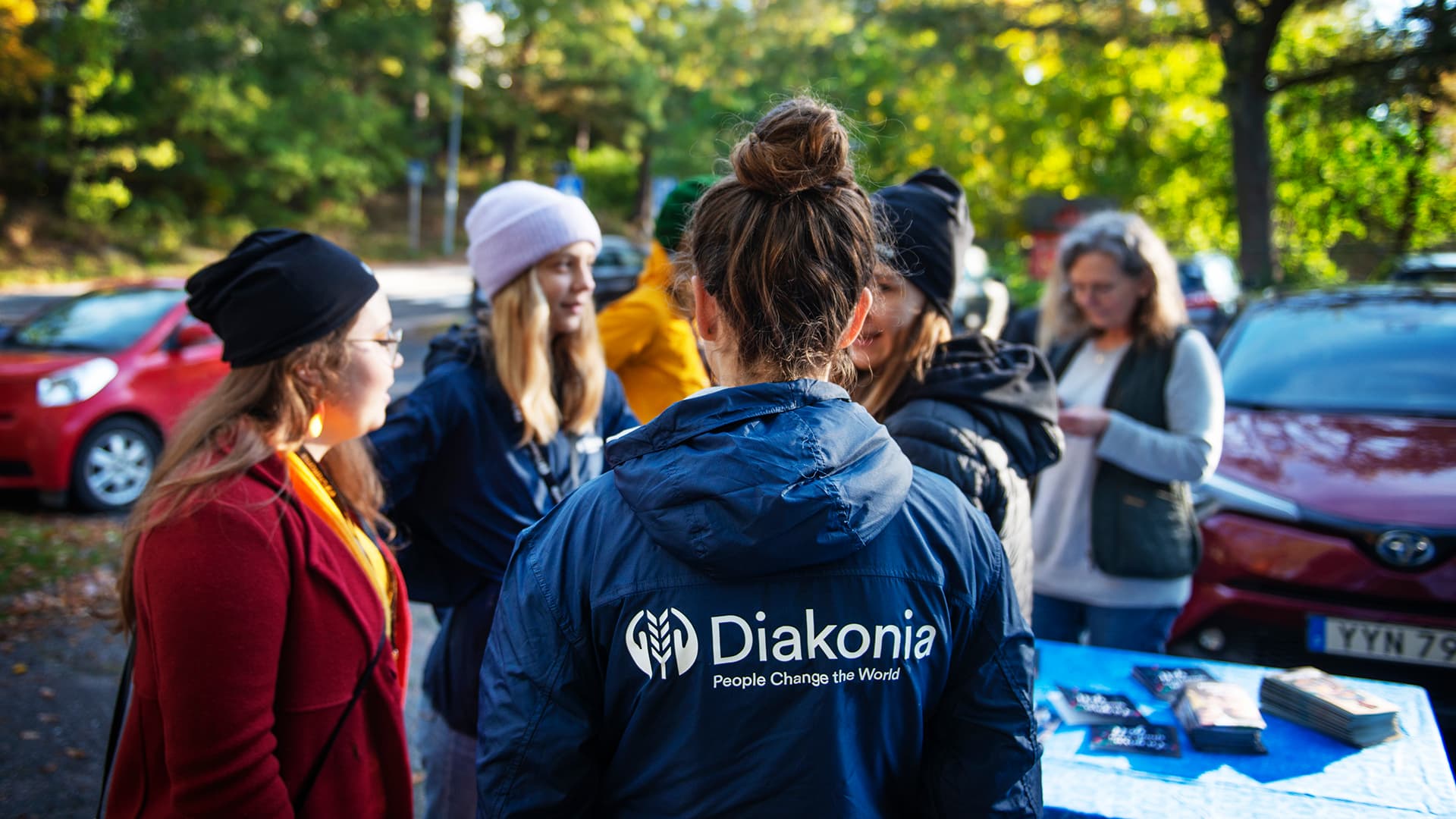 A person with their back against the camera, wearing a Diakonia jacket. In the background there are more people.