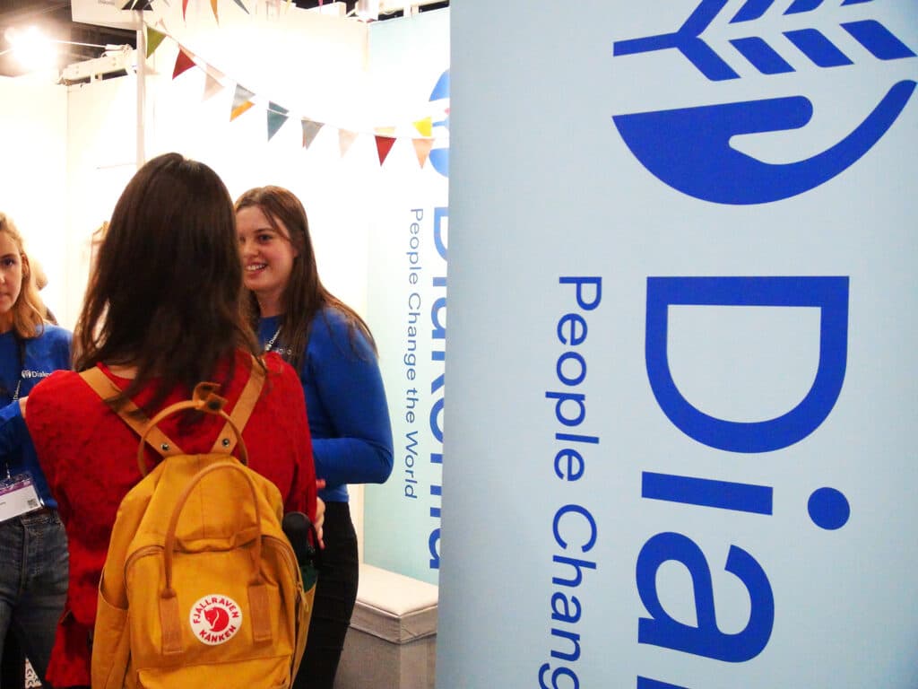 A large Diakonia sign and a person standing next to it with the back against the camera.