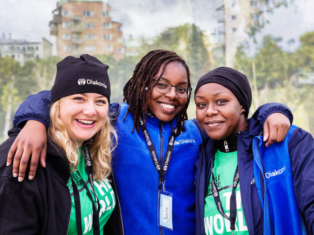 Three women wearing Diakonia jackets and hats, looking into the camera and smiling.