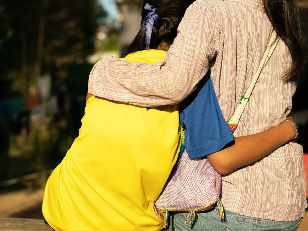 An adult and a child hugging, with their backs against the camera