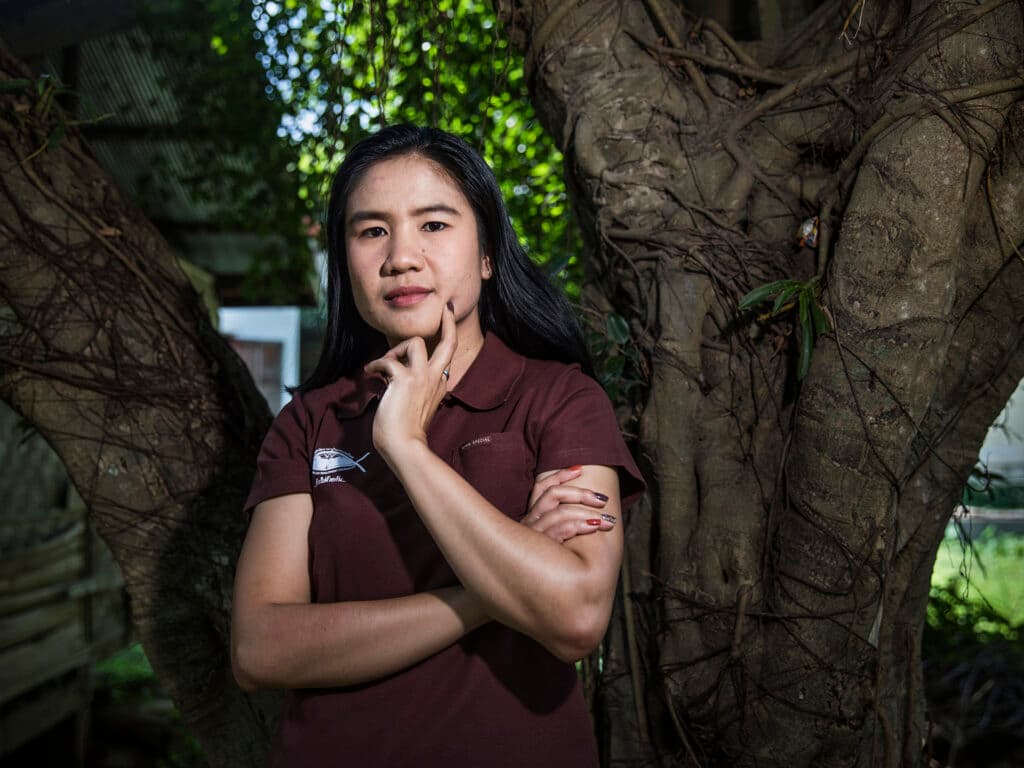 A woman looking into the camera, trees in the background.