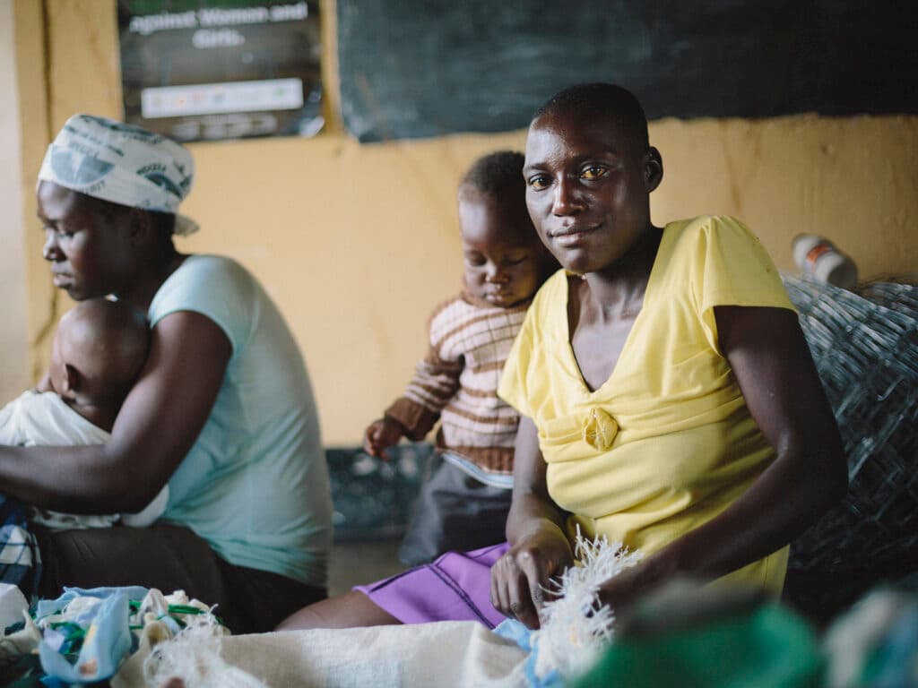 A Zimbabwean woman sitting on a floor sewing with her baby next to her.