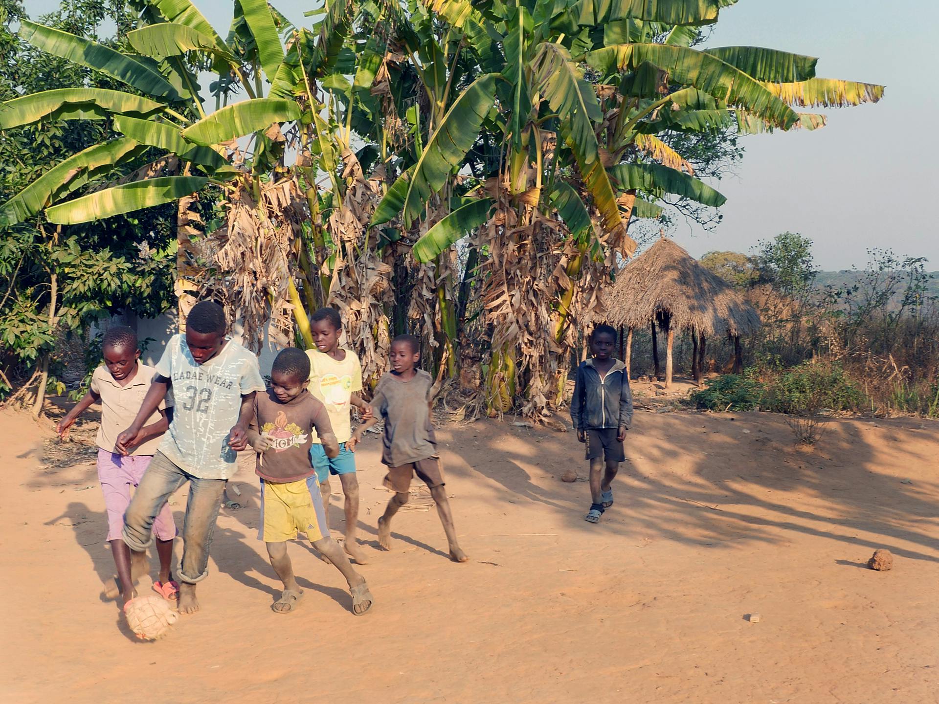 A group of kids playing football on dusty ground.