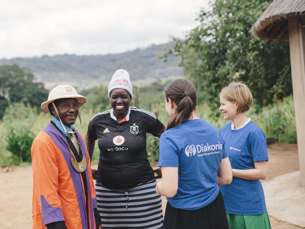 Two Diakonia employees wearing Diakonia t-shirts talking to a Zimbabwean couple