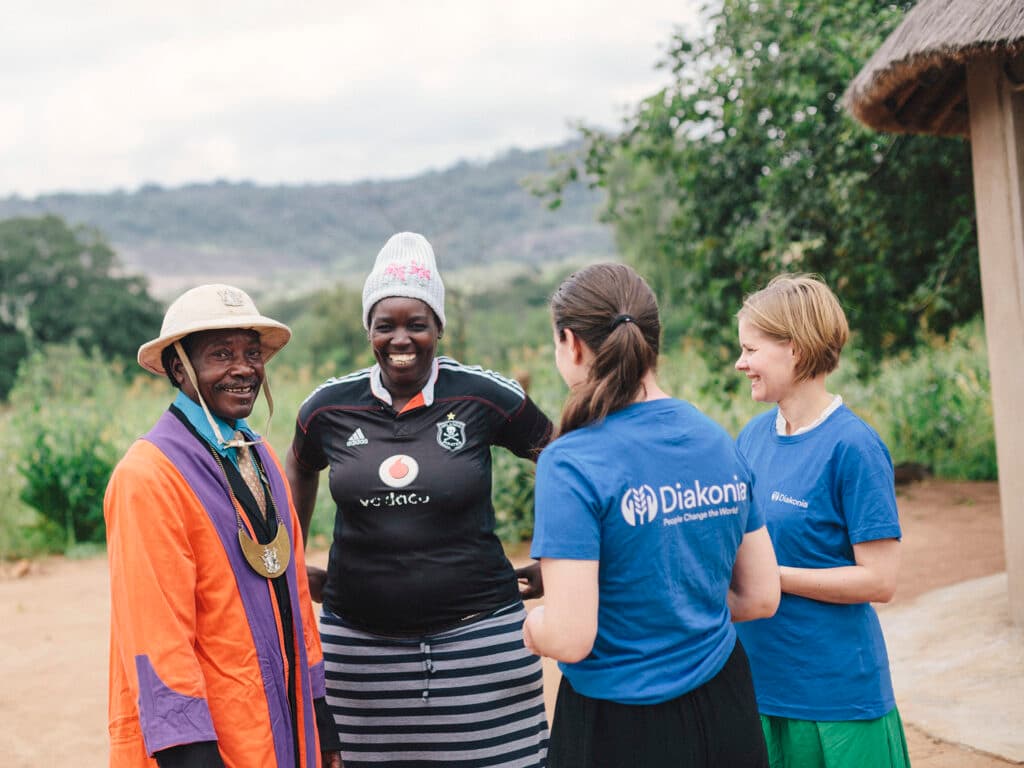 Two Diakonia employees wearing Diakonia t-shirts talking to a Zimbabwean couple