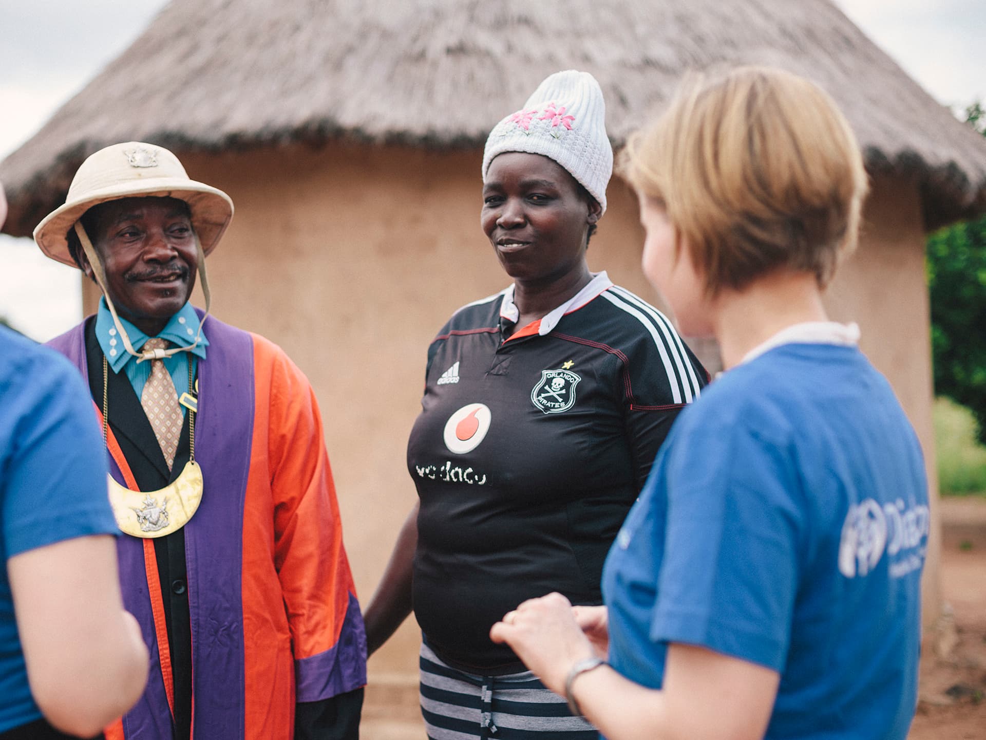 A person wearing a Diakonia t-shirt talking to a Zimbabwean couple.