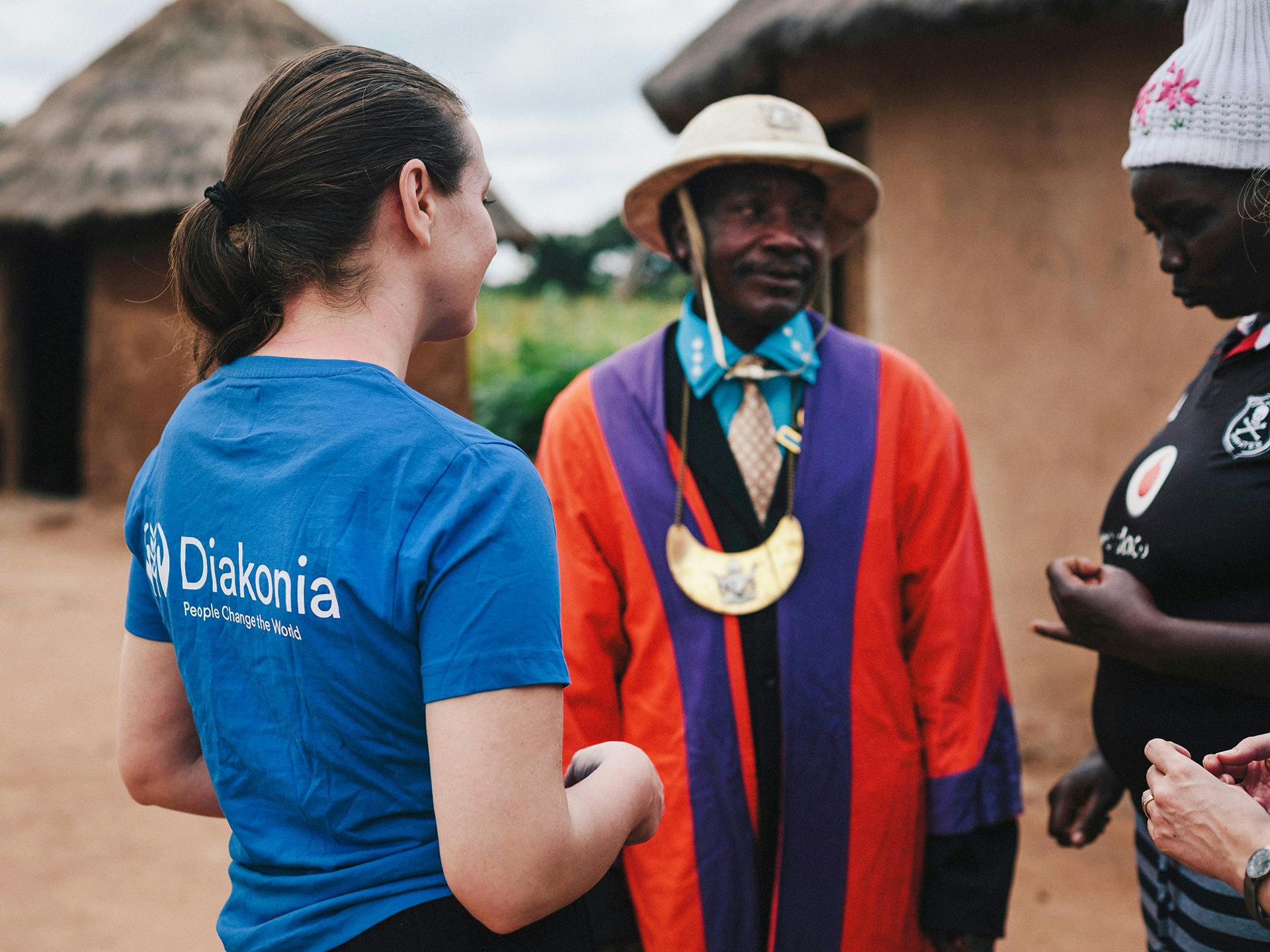 A woman with a Diakonia t-shirt with her back against the camera talking to two Zimbabwean men.