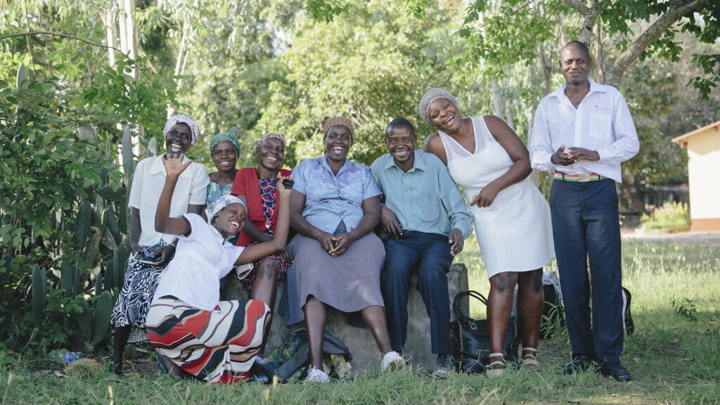 A group of Zimbabwean men and women outside in a green field with trees in the background.