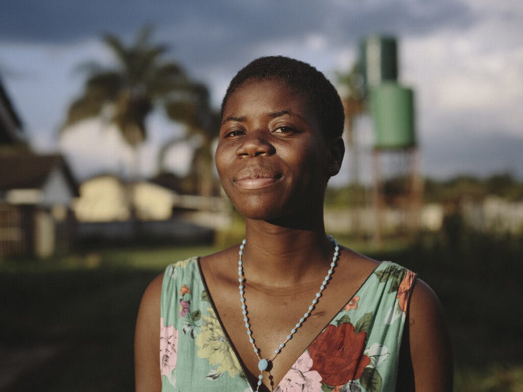 A portrait of a Zimbabwean woman in sunset. In the background there are some houses and trees.