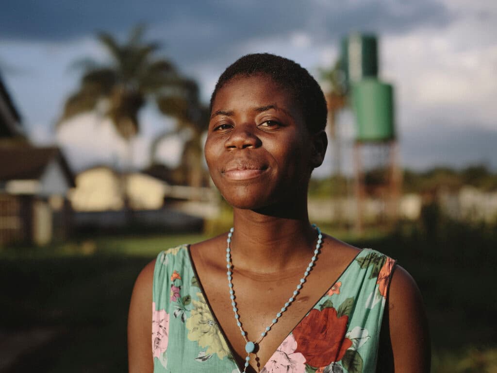 A portrait of a Zimbabwean woman in sunset. In the background there are some houses and trees.