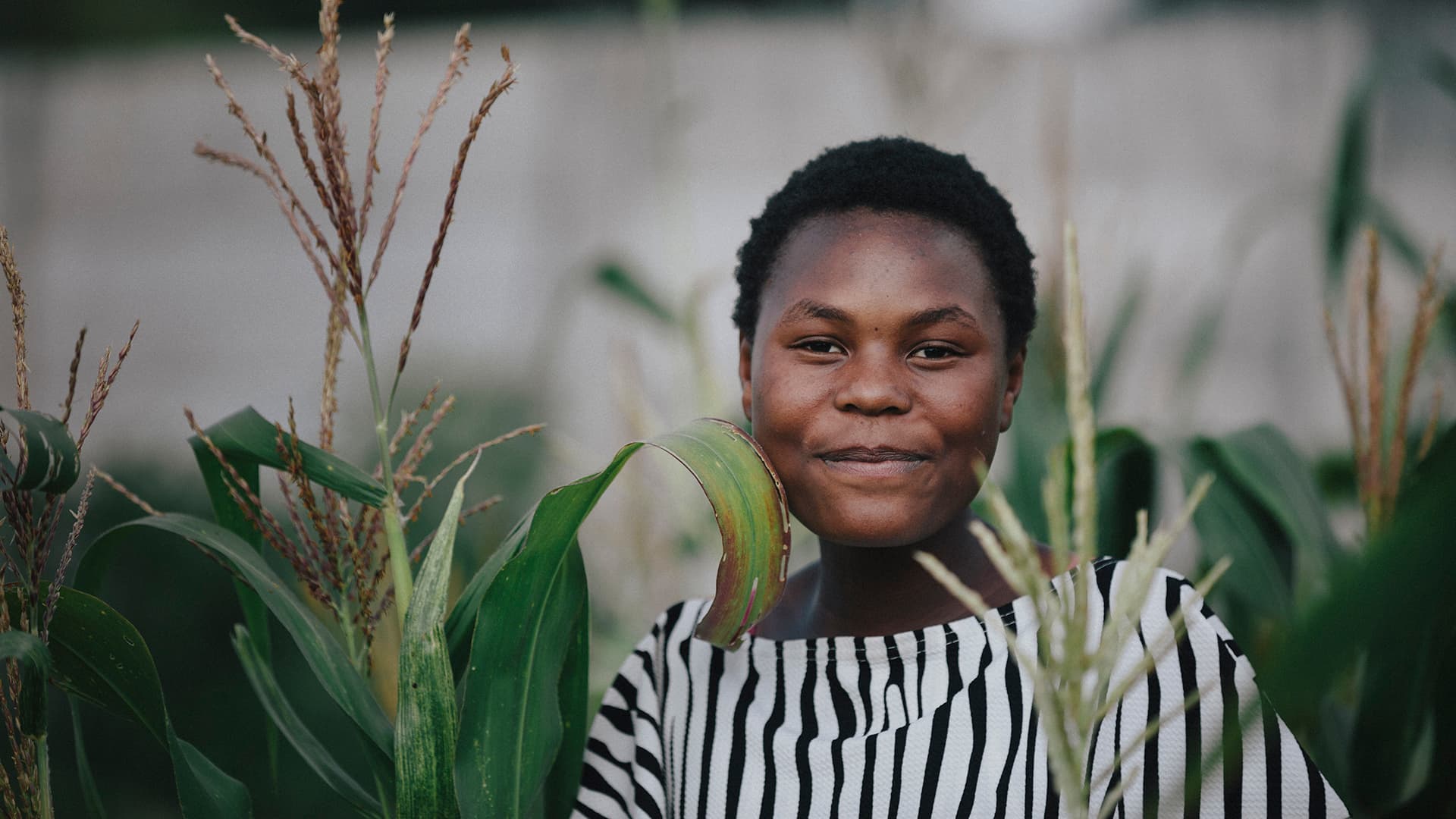 Zimbabwean woman standing in a field with green crops.