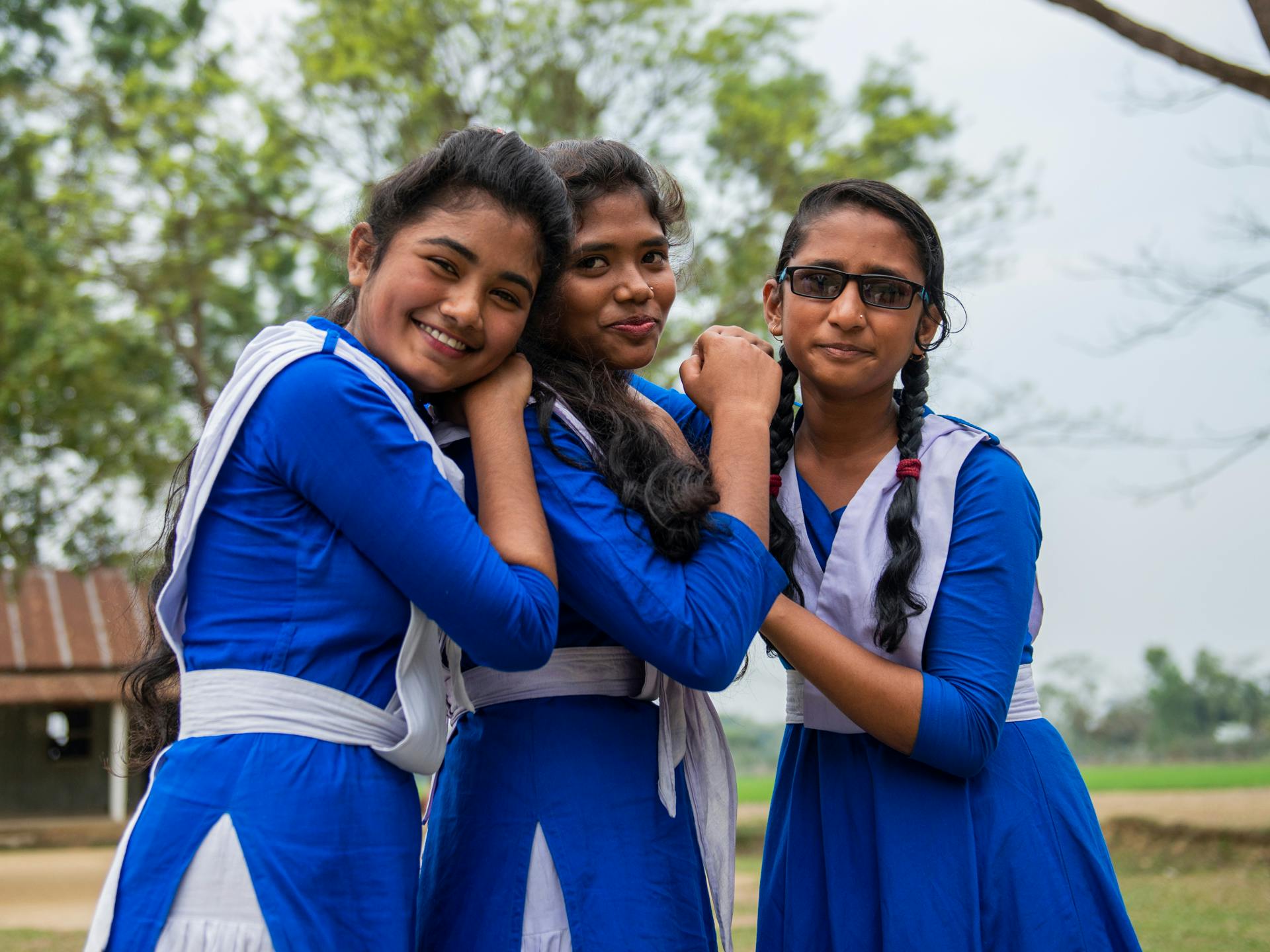 Three young women wearing blue and white school uniforms, standing together and smiling.