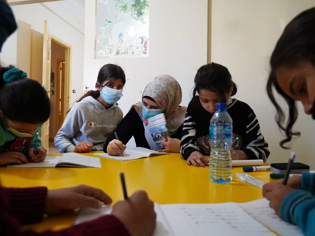 A group of young girls sitting by a table writing.