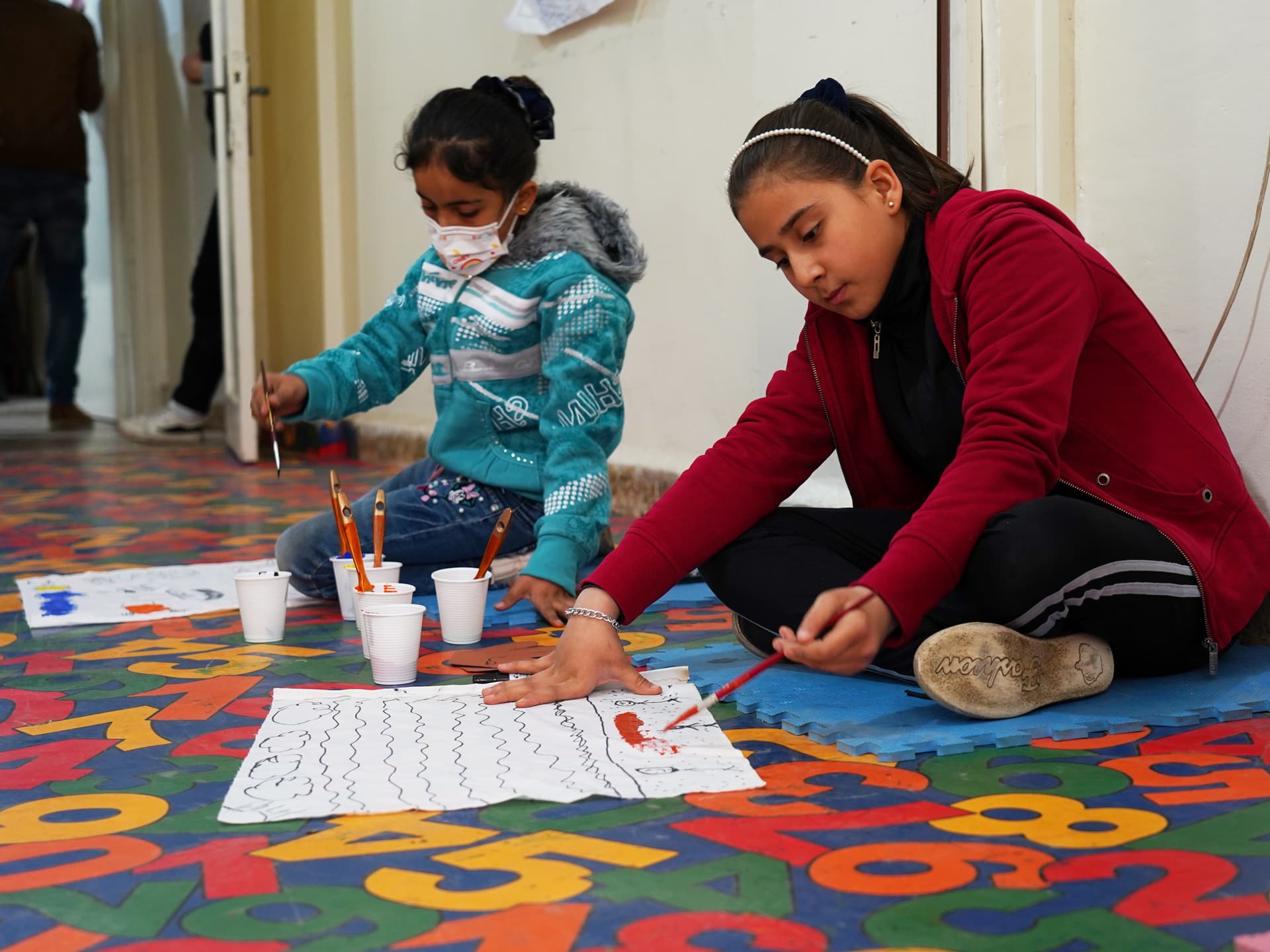 Two children sitting on the floor drawing.