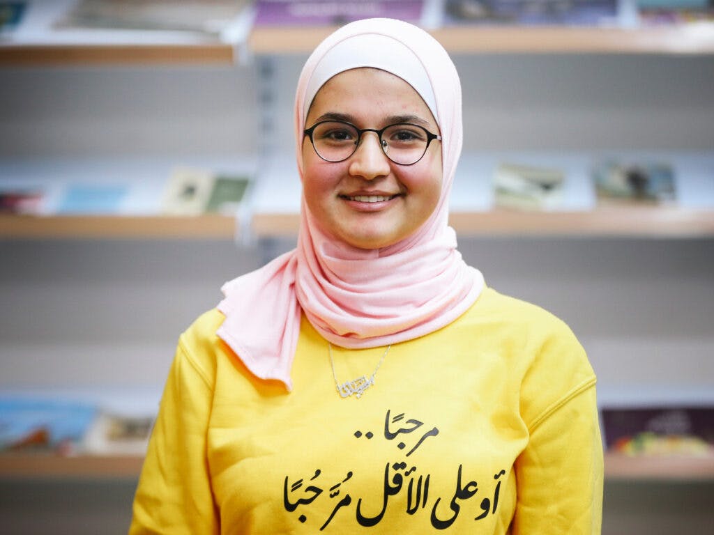 A young girl wering a hijab and a yellow t-shirt looking into the camera and smiling.
