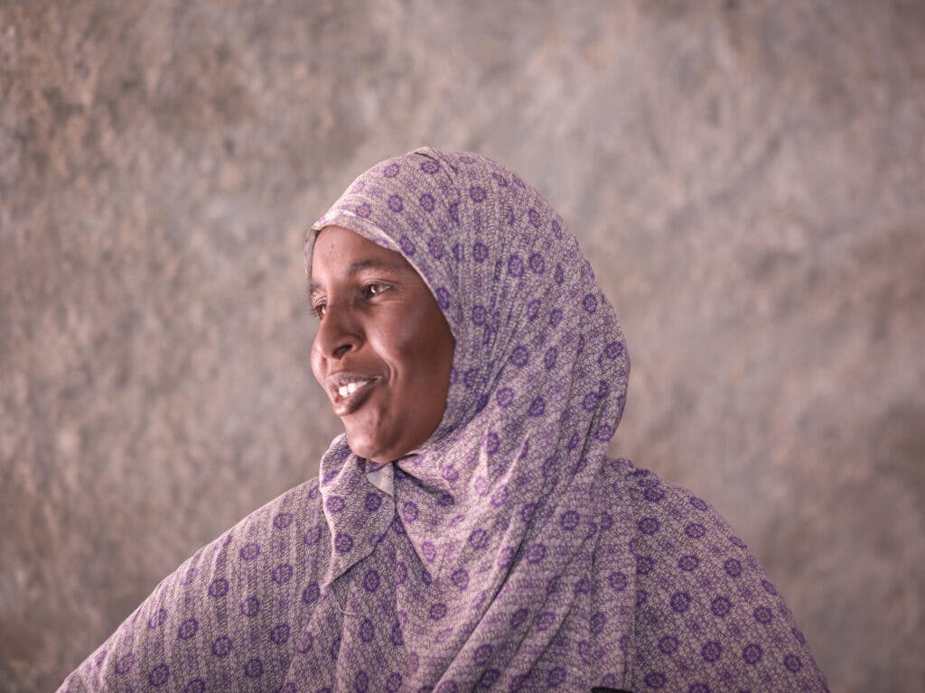 A woman in a purple hijab looking to the side and smiling.