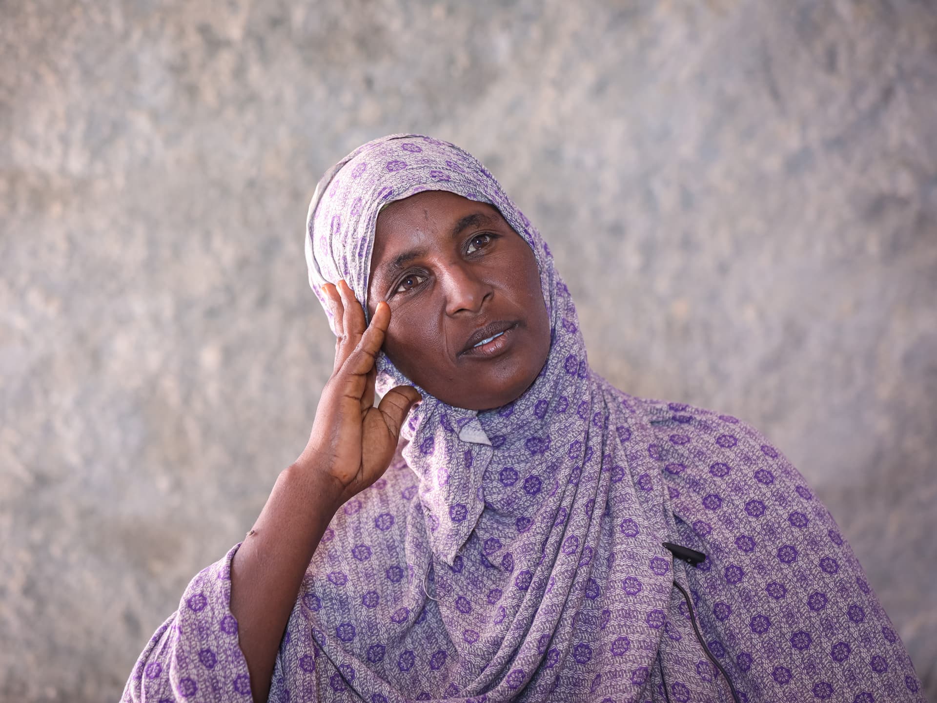 A woman wearing a purple hijab leaning her face in her hand.