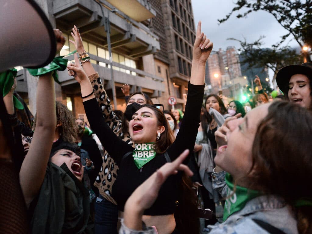 Photo: Lina Gasca A crowd of young women lifting their hands and screaming, wearing green scarves.