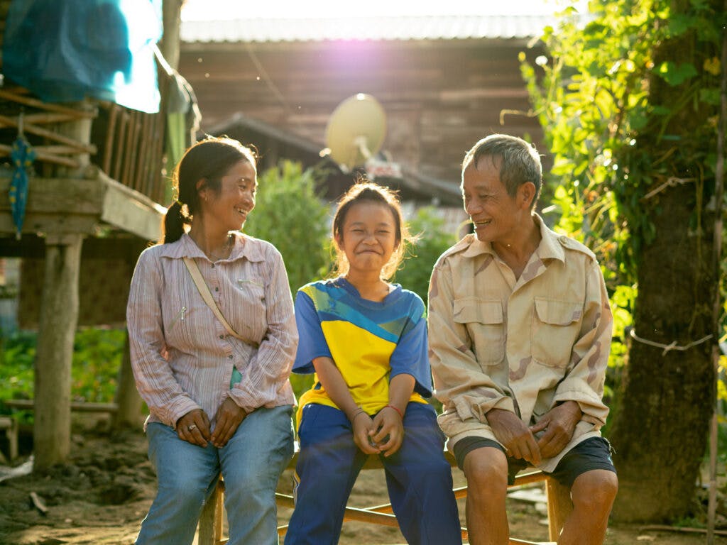 Three persons sitting outside, two adults and one child. They are smiling.