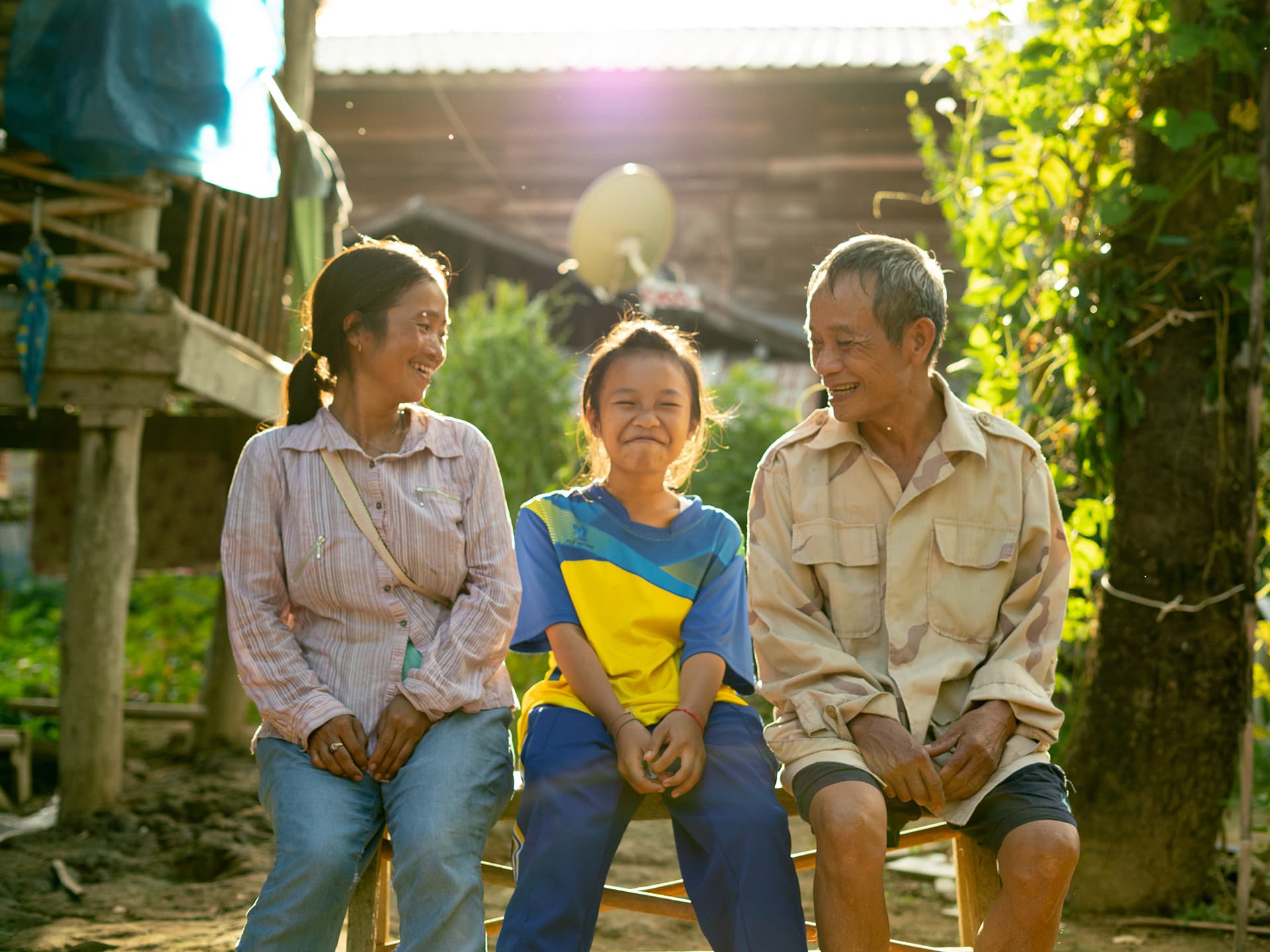 Photo: Diakonia Three persons sitting outside, two adults and one child. They are smiling.