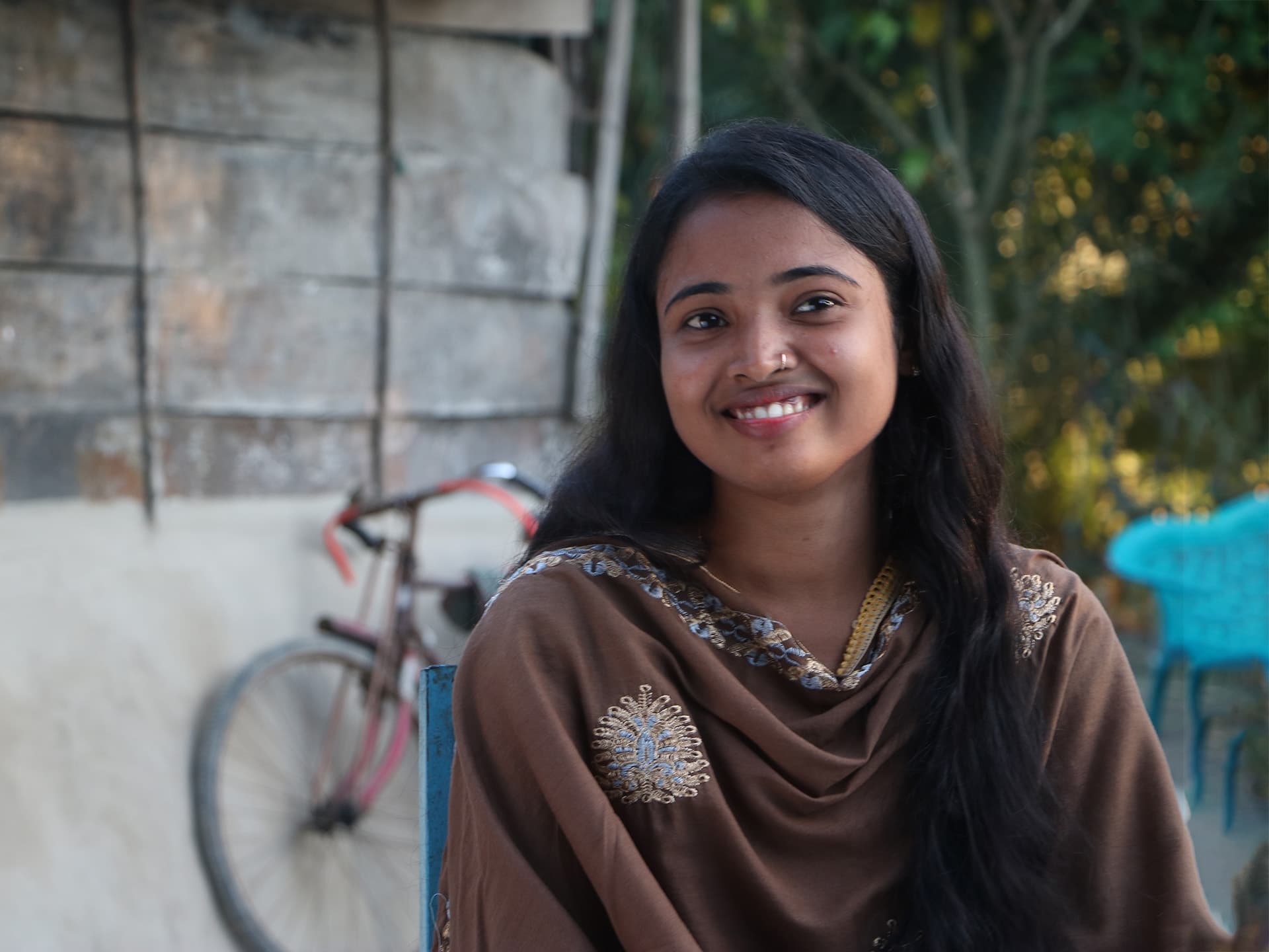 A young girl wearing a brown top, looking into the camera smiling.