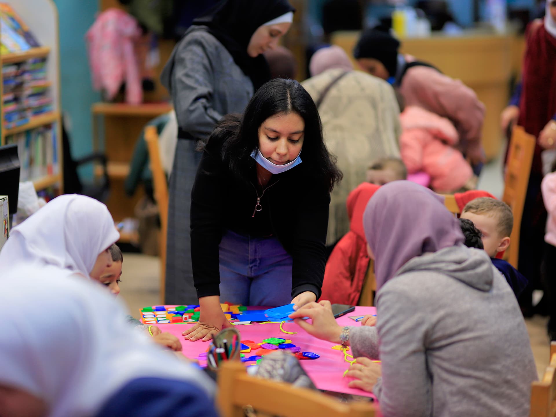 A girl sitting on a floor with art material in front of her. There is a lot of people around her.